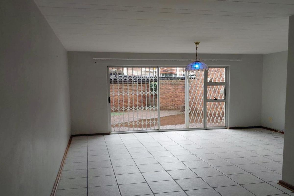 An empty living room featuring tiled flooring and a sliding glass door with a security gate, providing direct access to the rear patio area.