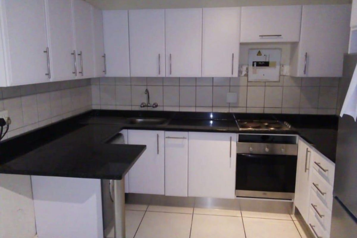 A clean, functional kitchen featuring white cabinetry, black granite countertops, a built-in oven, electric hob, and a convenient breakfast bar.