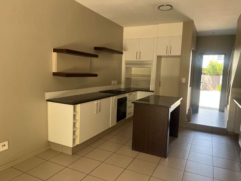 A functional kitchen featuring white cabinetry, dark granite countertops, a built-in oven, hob, and a central island, with tiled flooring throughout.