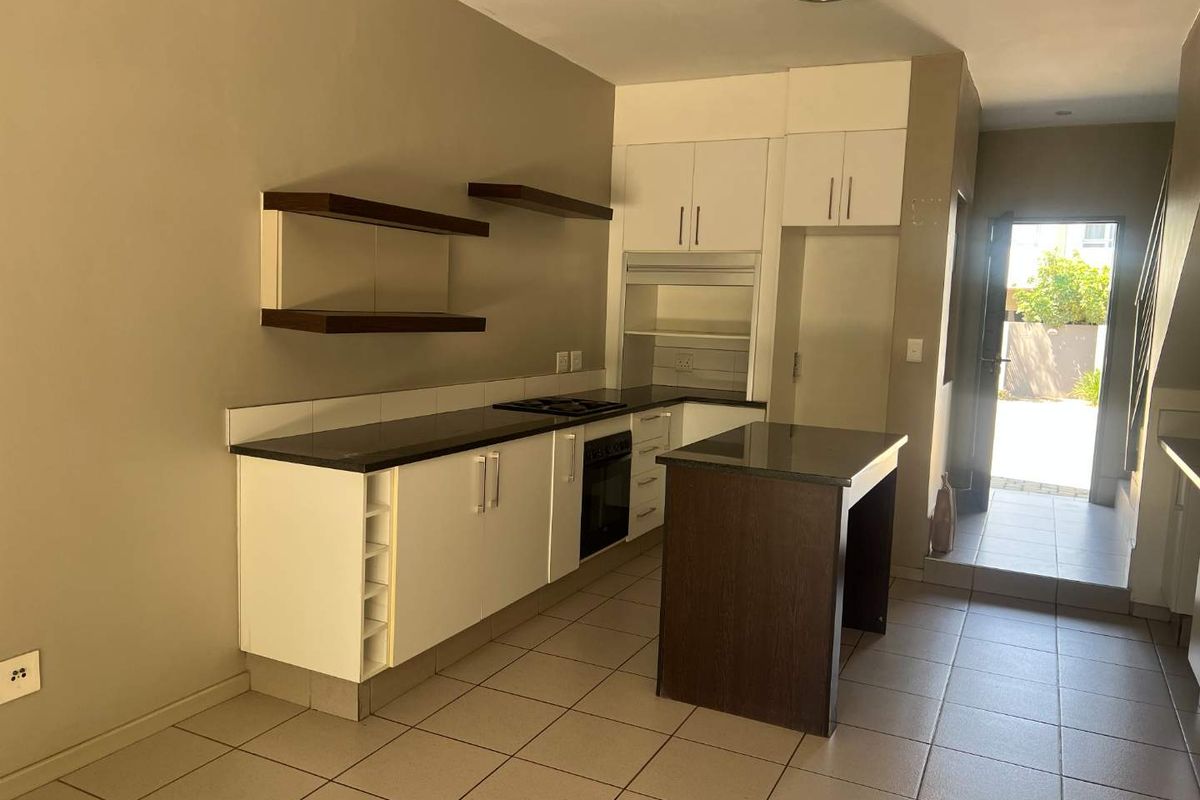 A functional kitchen featuring white cabinetry, dark granite countertops, a built-in oven, hob, and a central island, with tiled flooring throughout.