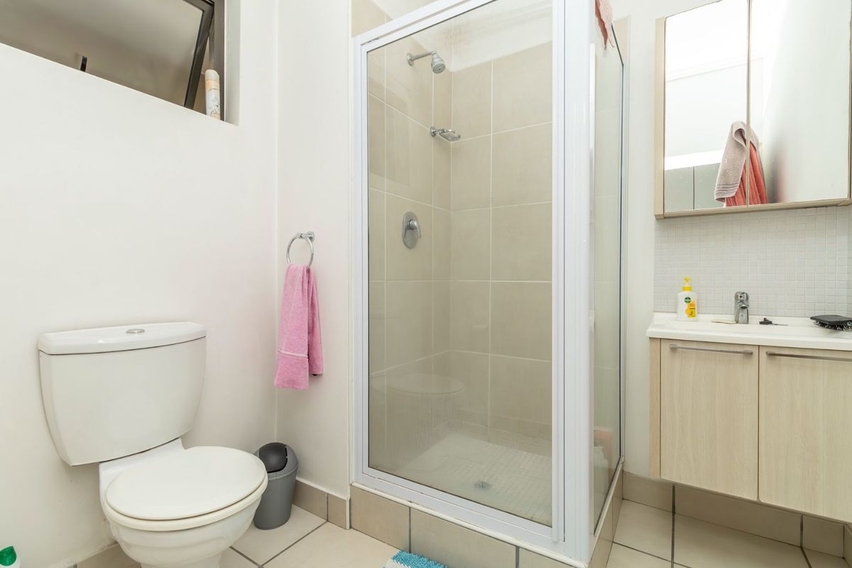 A functional bathroom featuring a glass-enclosed shower, a modern vanity with basin, and a standard toilet, finished with neutral wall and floor tiles.