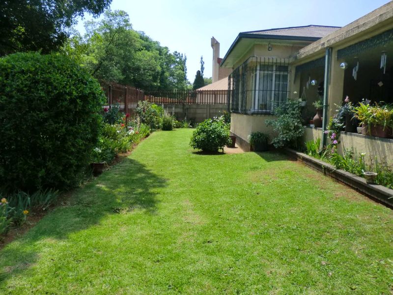 A well-maintained rear garden featuring a manicured lawn, established landscaping, and a covered patio area adjacent to the main house structure.