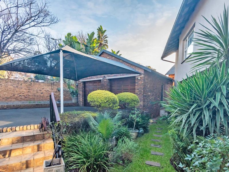 Front exterior view featuring a double brick garage, paved driveway with shade sail, and landscaped garden with stone steps leading to the entrance.