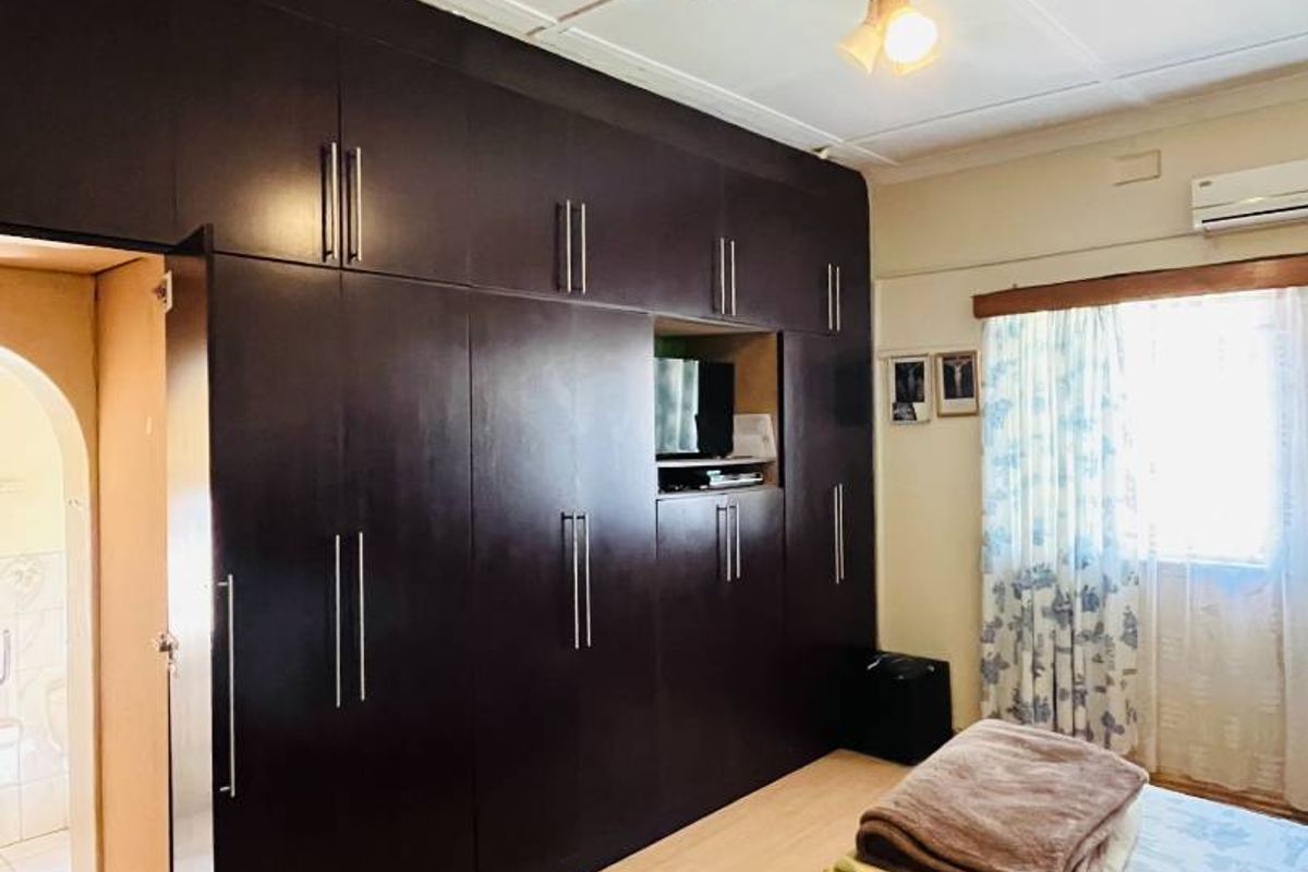 Bedroom featuring extensive floor-to-ceiling dark wood built-in cabinetry, light wood-look flooring, ceiling fan, and an integrated air conditioning unit.