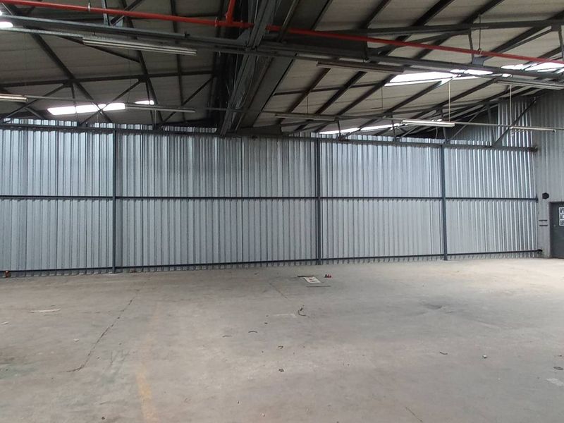 Spacious industrial warehouse unit featuring high ceilings with exposed steel trusses, corrugated metal wall cladding, and durable concrete flooring.