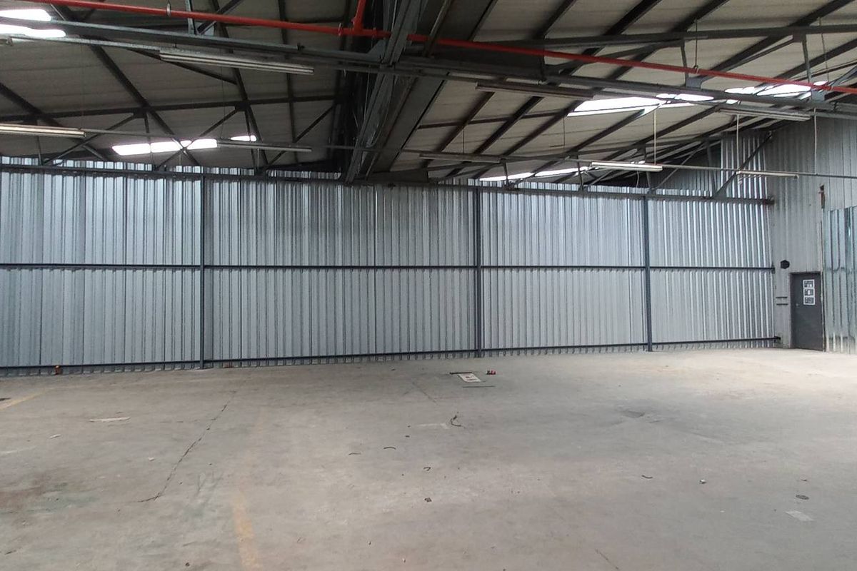 Spacious industrial warehouse unit featuring high ceilings with exposed steel trusses, corrugated metal wall cladding, and durable concrete flooring.