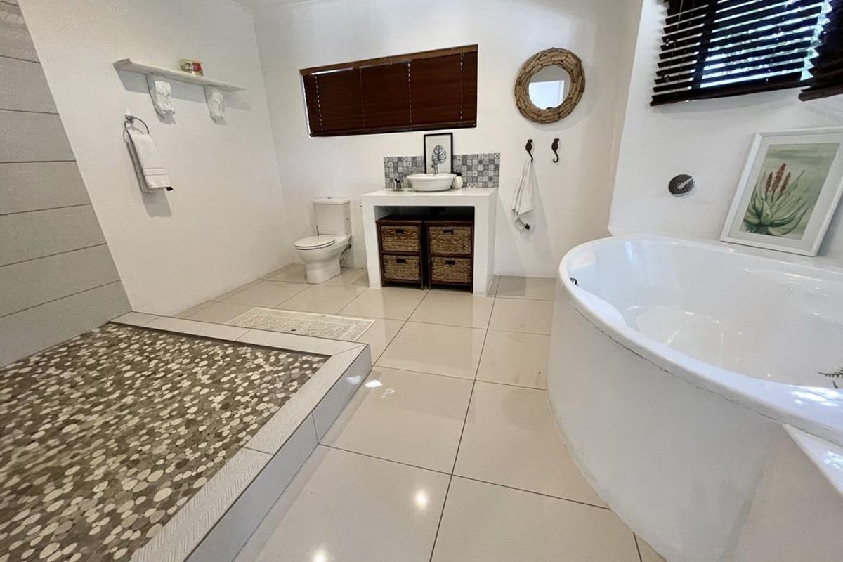 Spacious bathroom featuring a walk-in shower with pebble flooring, a built-in vanity with vessel sink, a toilet, and a large soaking bathtub.