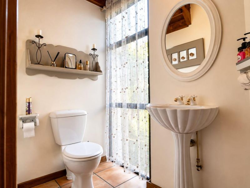 A well-maintained bathroom featuring a classic pedestal sink, a standard toilet, and tiled flooring, illuminated by a large window with natural light.