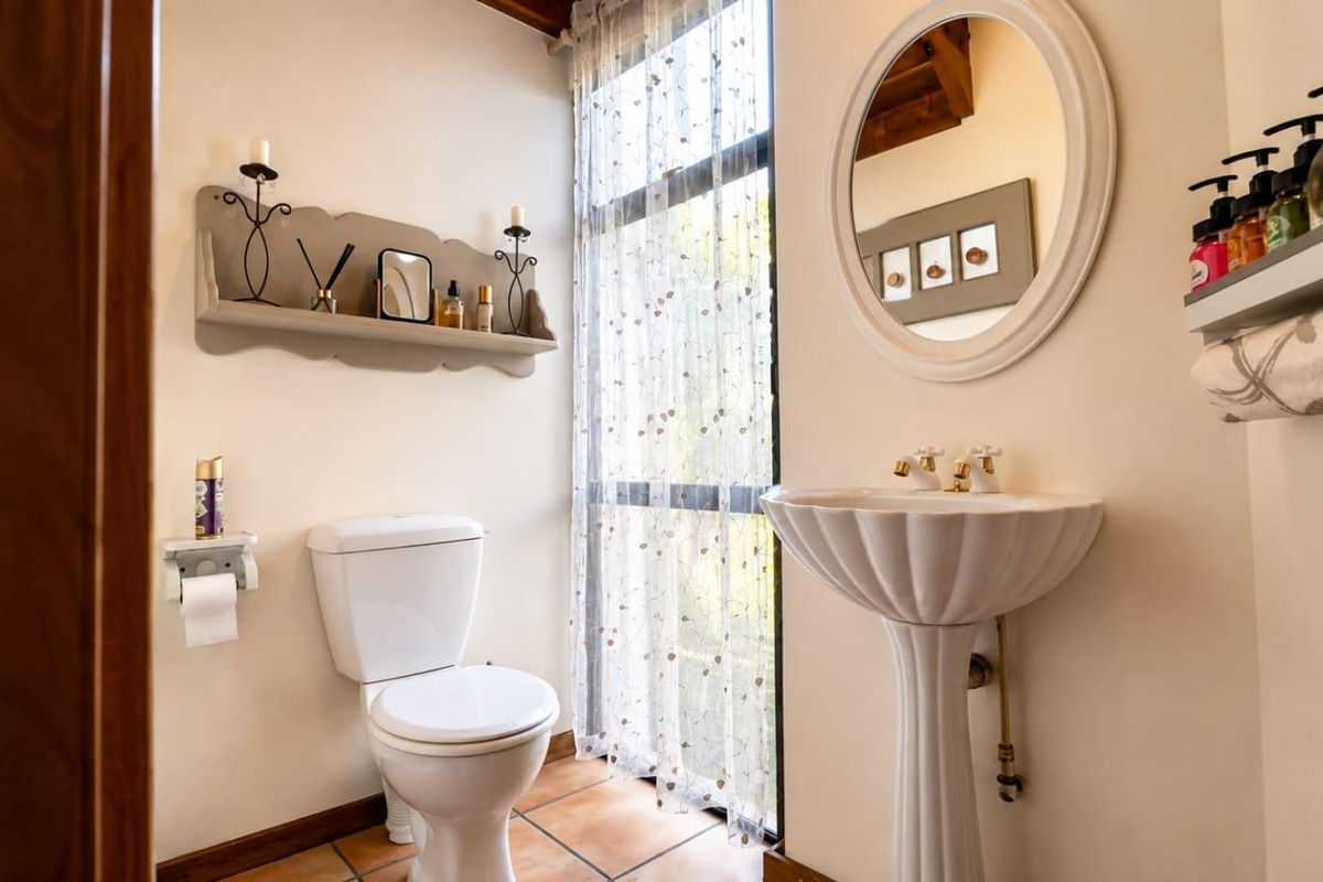 A well-maintained bathroom featuring a classic pedestal sink, a standard toilet, and tiled flooring, illuminated by a large window with natural light.
