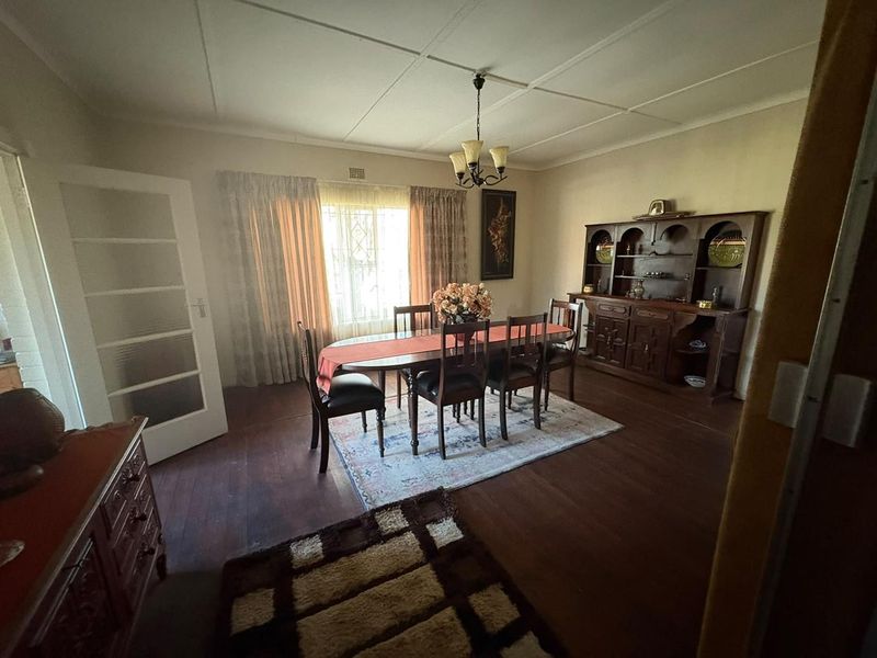 A traditional dining room featuring hardwood flooring, a central light fixture, and a window with security bars, offering a classic layout.