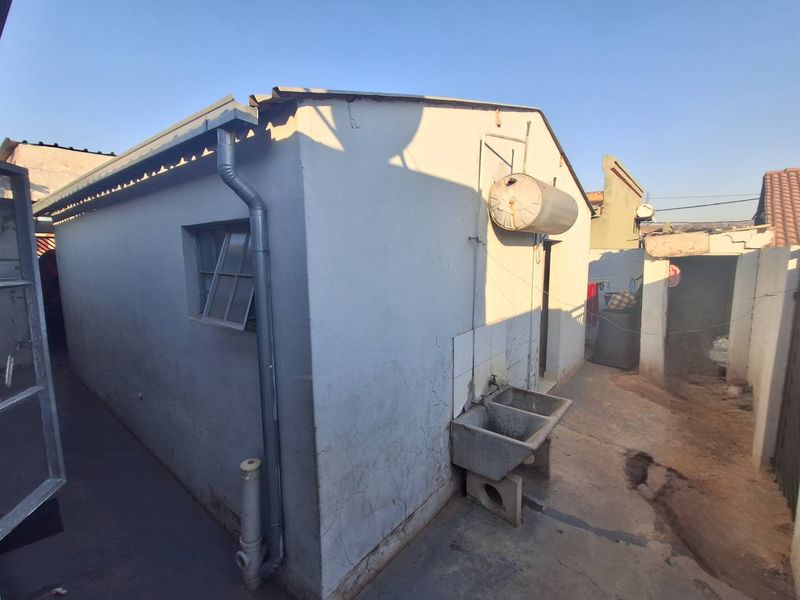 Rear exterior view of the property featuring a concrete wash trough, external plumbing, and an externally mounted electric geyser.