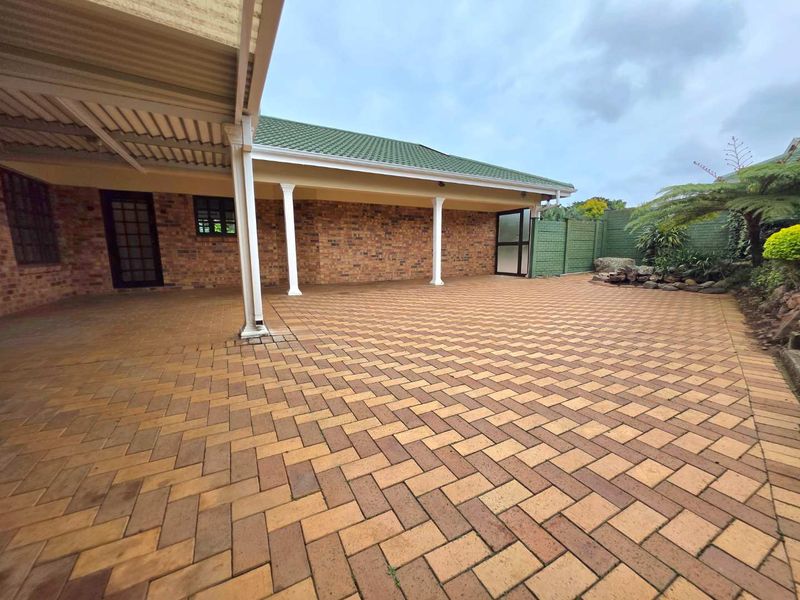 A spacious covered patio area featuring brick paving, structural support columns, and a brick facade, providing a functional outdoor entertainment space.