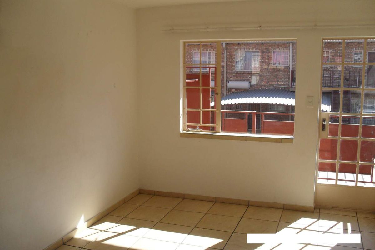 An empty living area featuring tiled flooring, natural light, and direct access to an exterior space through a steel-framed glass door.
