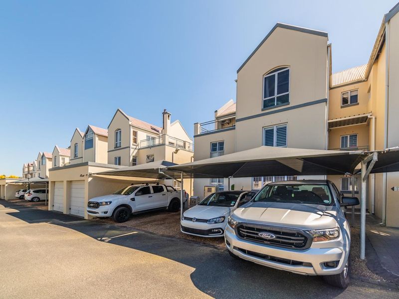 Exterior view of an apartment complex featuring covered parking bays, garages, and multi-story residential units with balconies.