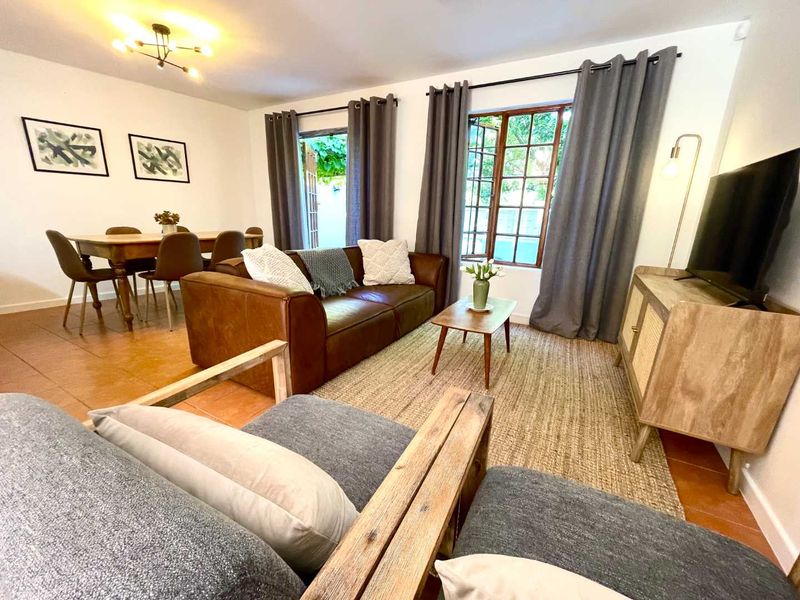 Open-plan living and dining area featuring terracotta floor tiles, timber-framed windows, and direct access to the outdoor space through French doors.
