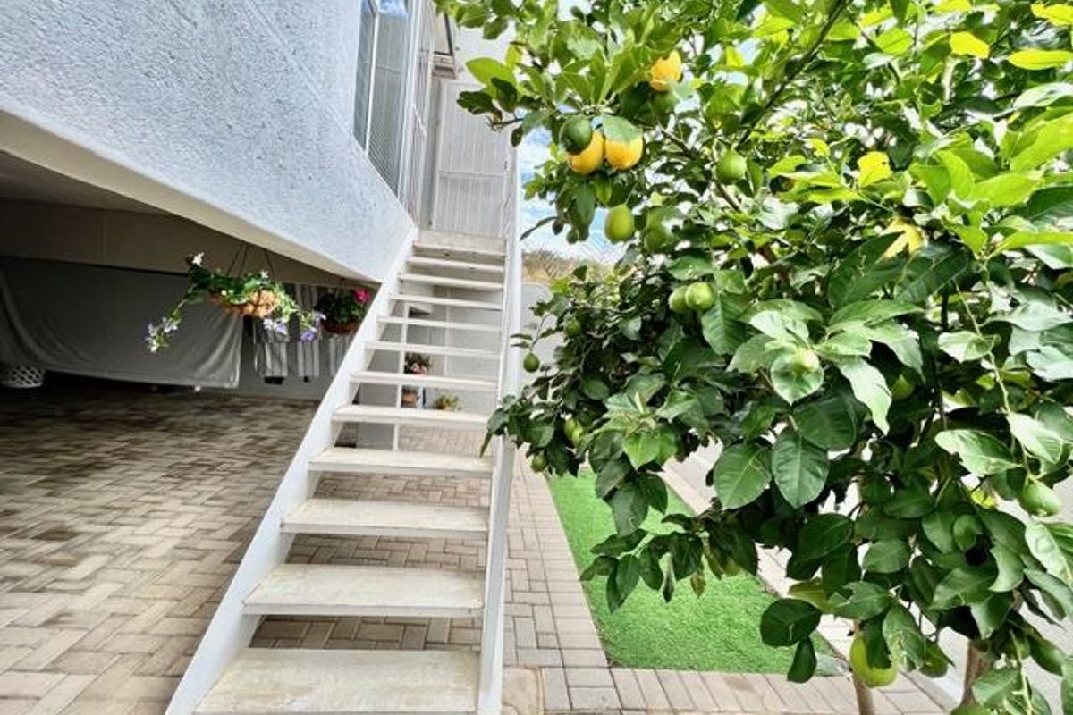 Rear exterior view featuring a paved patio area, artificial lawn, and an external staircase leading to the upper level of the townhouse.