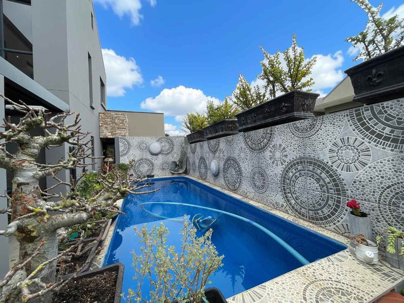 A well-maintained swimming pool area featuring a unique decorative tiled boundary wall and modern stone cladding accents.