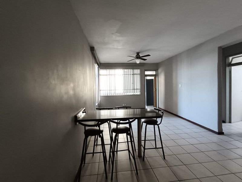 Open plan living area featuring tiled flooring, a ceiling fan, and a wall-mounted breakfast bar, with visible signs of ceiling water damage.