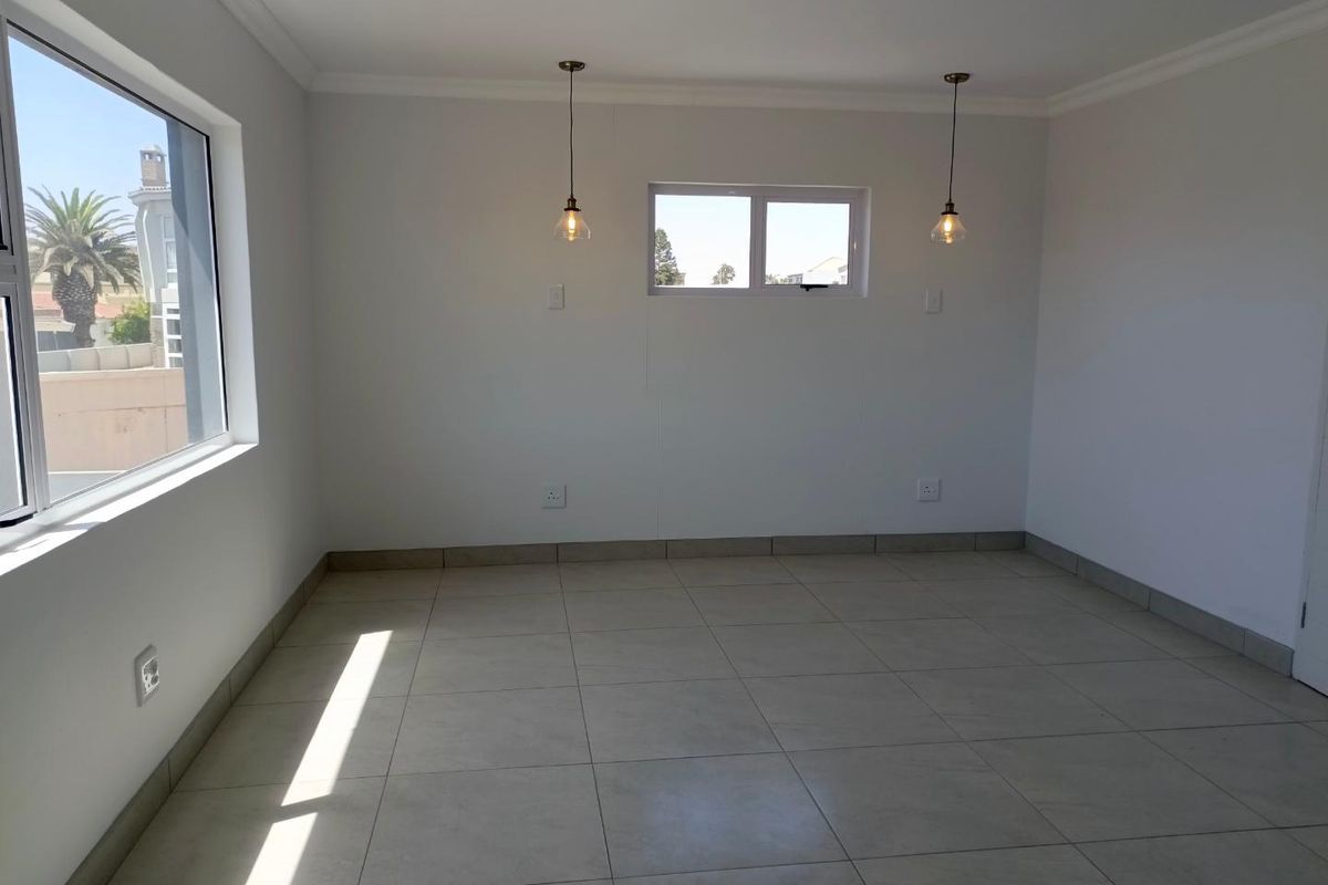 A bright, empty living area featuring neutral floor tiles, recessed ceiling lighting, and modern pendant lights, offering a clean and versatile space.