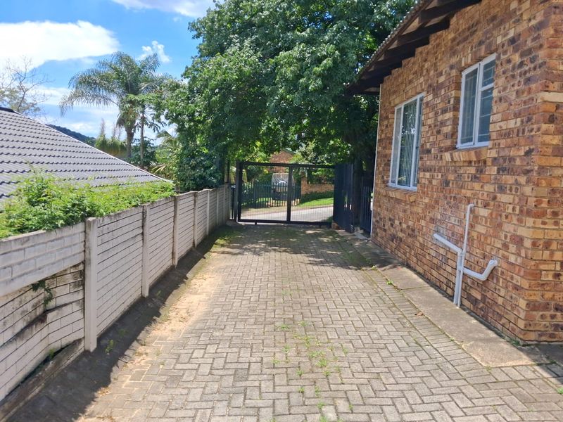 A side view of the property featuring a paved driveway, face brick exterior walls, and a secure metal gate entrance.