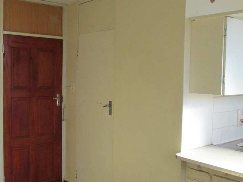 An empty kitchen area featuring dated cabinetry, tiled backsplash, and dark floor tiles, offering a blank canvas for potential renovation and modernization.
