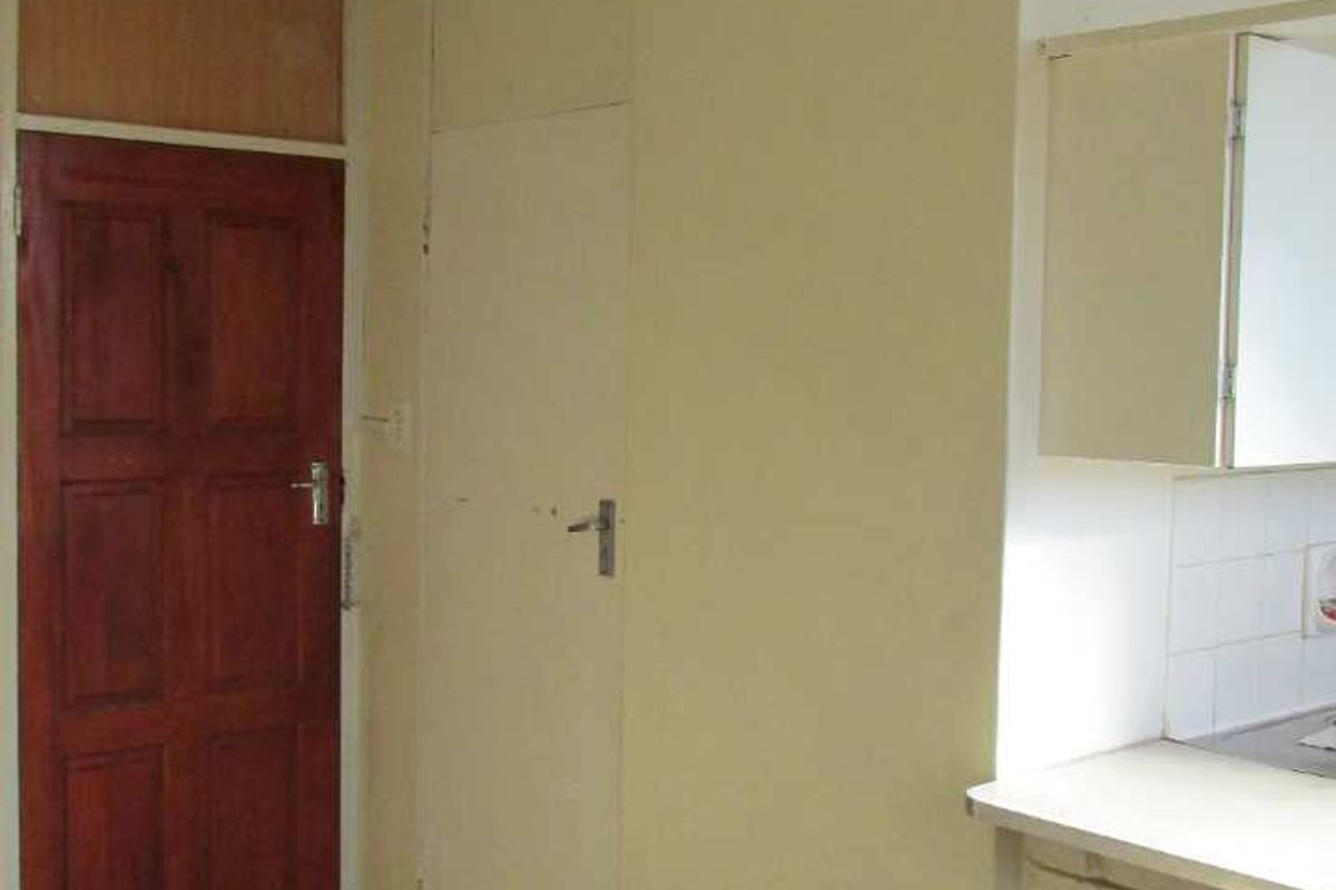 An empty kitchen area featuring dated cabinetry, tiled backsplash, and dark floor tiles, offering a blank canvas for potential renovation and modernization.