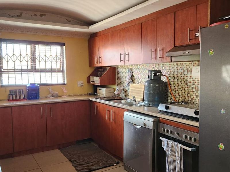 A functional kitchen featuring wooden cabinetry, tiled backsplash, and tiled flooring, requiring some cosmetic ceiling repairs to enhance its overall appeal.