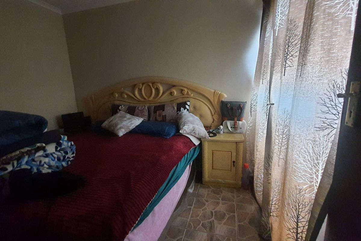 A bedroom featuring tiled flooring and a window with curtains, providing a functional sleeping space.
