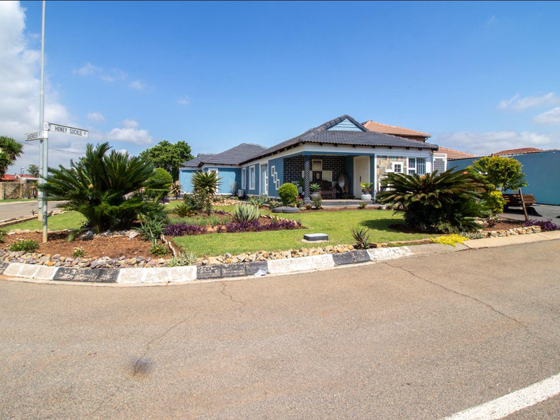 A well-maintained single-story residential property on a corner lot, featuring a tiled roof, covered entrance porch, and established landscaped garden.