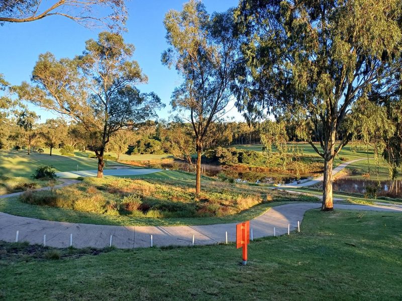 A scenic view overlooking a golf course with a water feature, mature trees, and a paved pathway winding through the landscape.