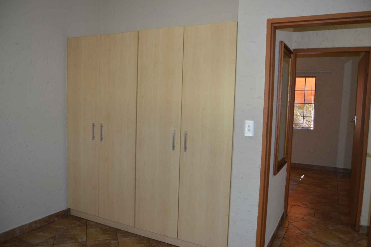 A bedroom interior featuring built-in light wood cabinetry and tiled flooring, with a doorway leading to an adjacent room.