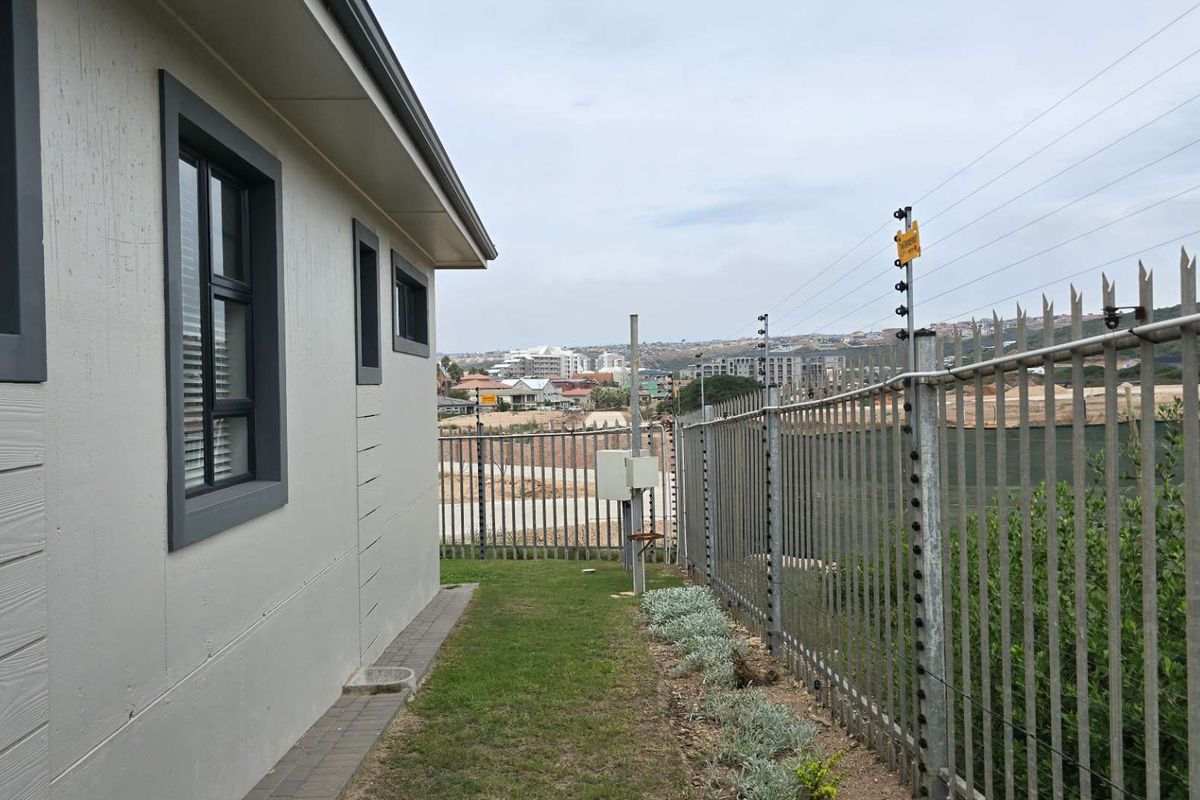Side exterior view of the property featuring a paved walkway, manicured lawn, and secure perimeter fencing with an integrated electric fence system.