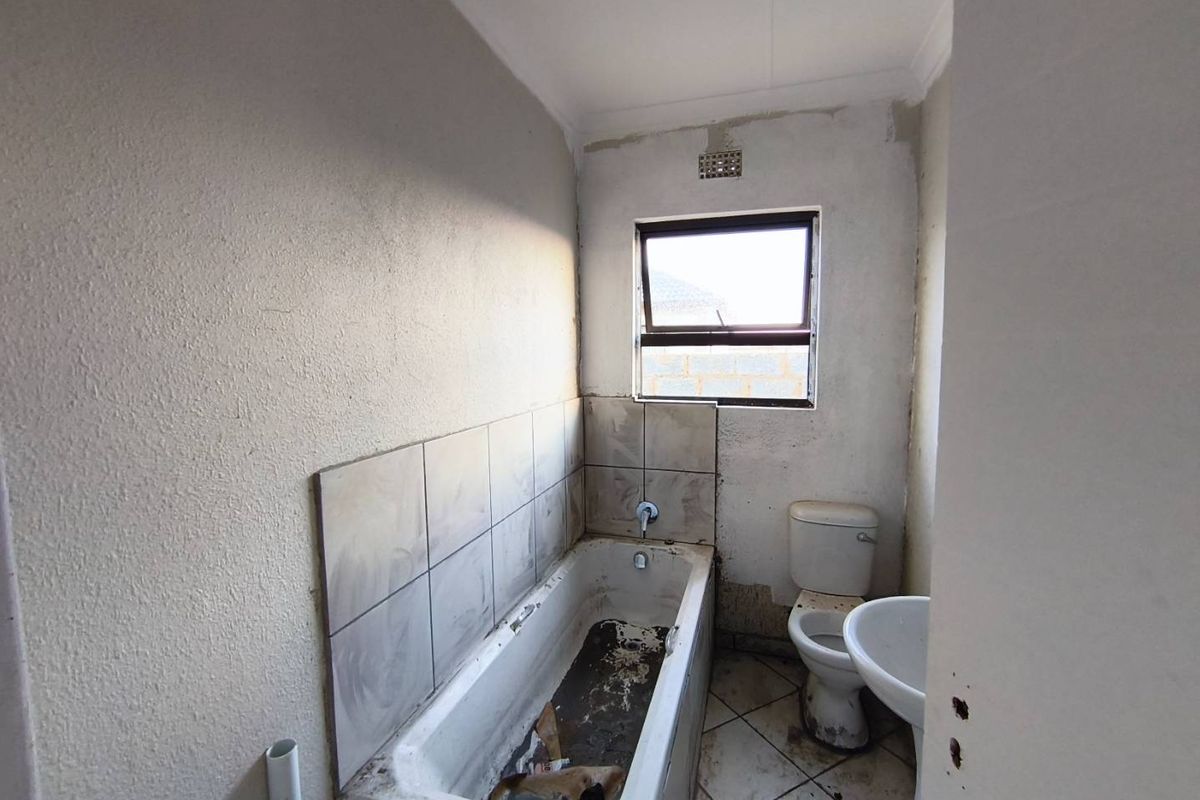 A small bathroom in need of significant renovation, featuring a bathtub, toilet, and pedestal basin with unfinished wall finishes and worn flooring.