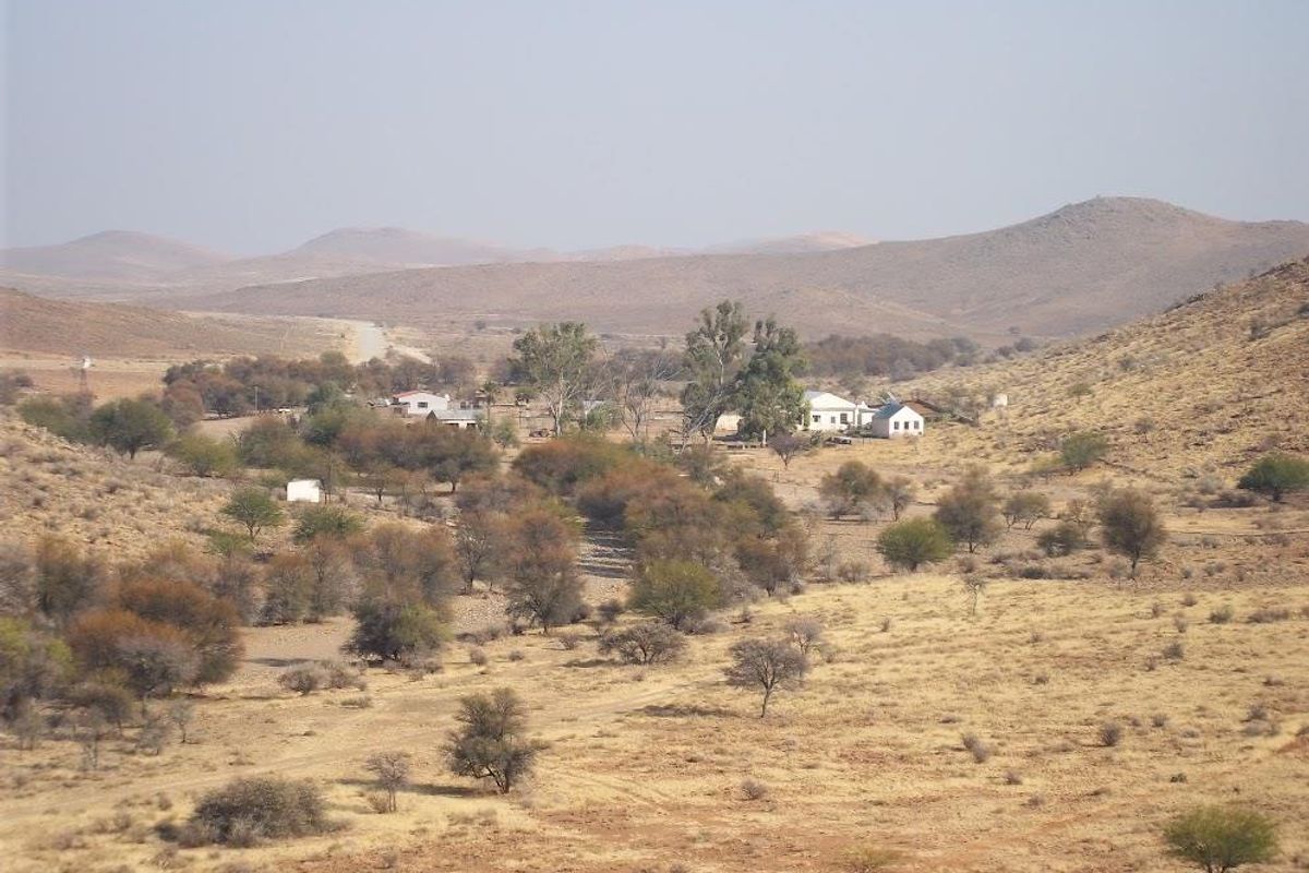 An elevated aerial view of a rural farm property set within a vast, arid landscape featuring rolling hills and sparse vegetation.