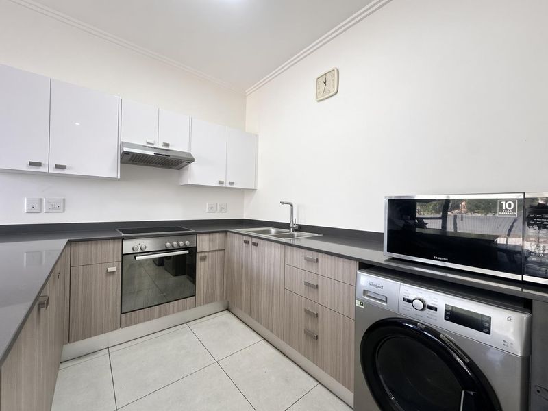 A modern, well-maintained kitchen featuring light wood-grain cabinetry, stone countertops, integrated oven and hob, and tiled flooring.