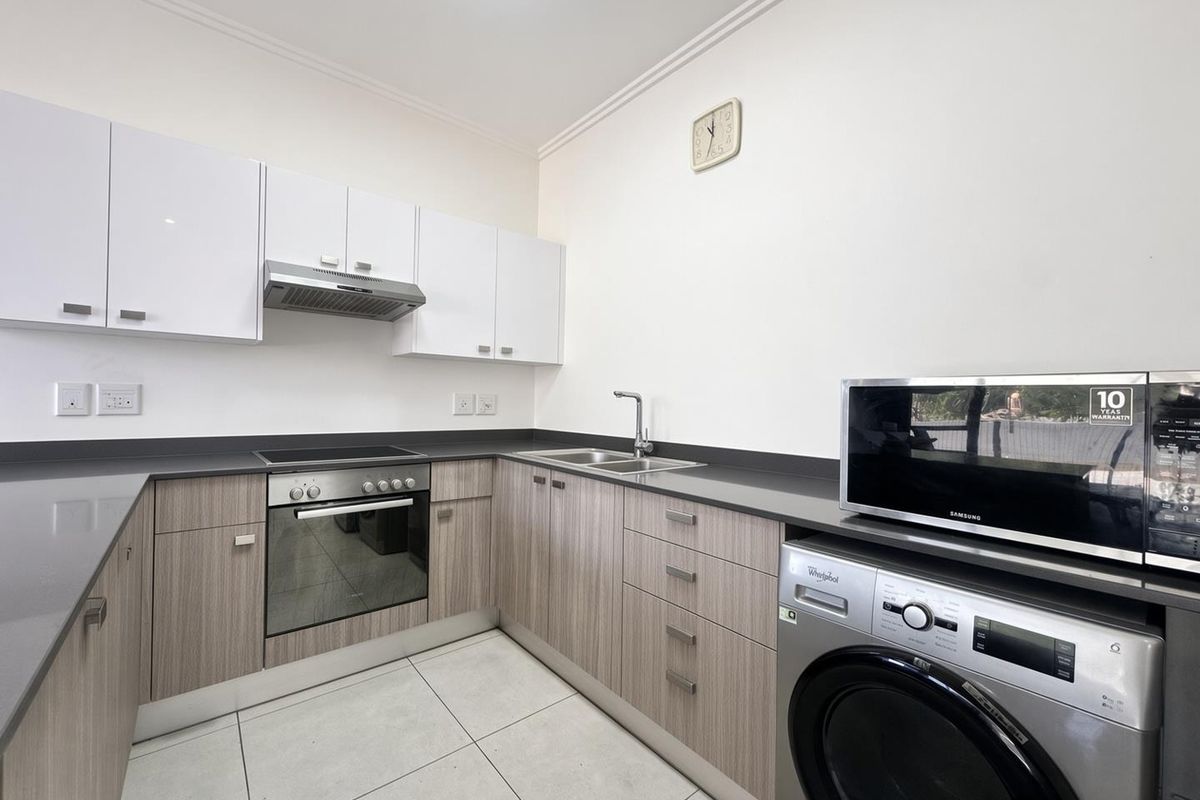 A modern, well-maintained kitchen featuring light wood-grain cabinetry, stone countertops, integrated oven and hob, and tiled flooring.