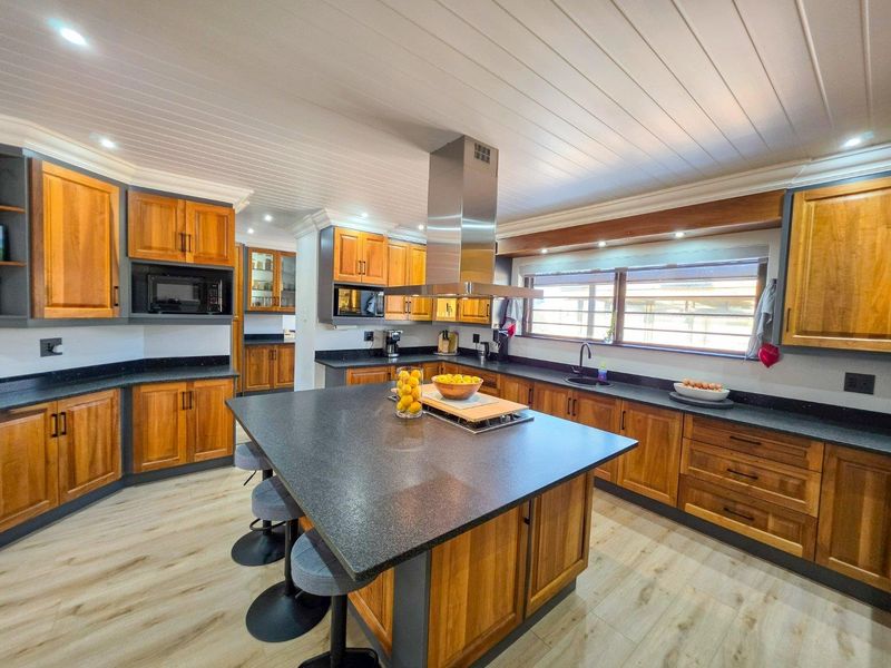 Spacious kitchen featuring warm wooden cabinetry, dark granite countertops, a large central island with breakfast seating, and a modern stainless steel extractor fan.
