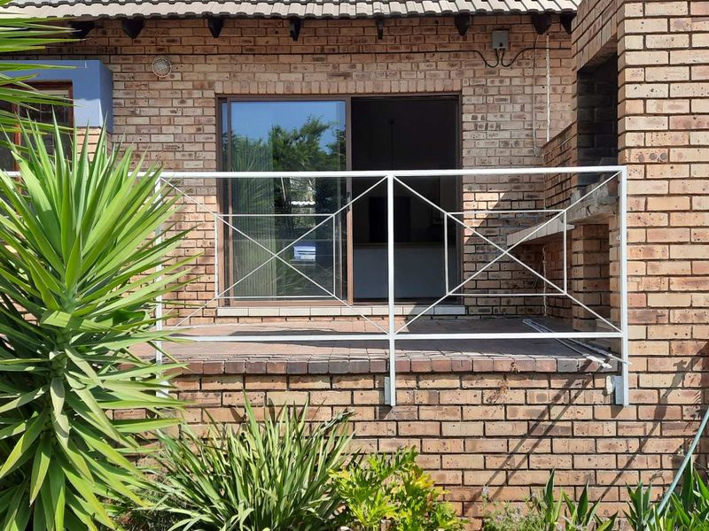 A brick-built patio area featuring a built-in braai, metal safety railing, and sliding door access to the interior living space.