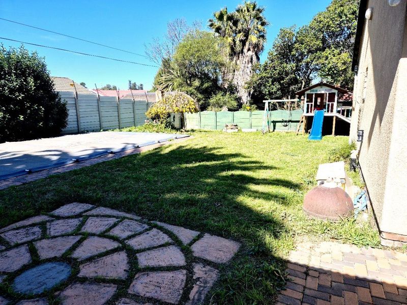 A rear garden area featuring a lawn, a paved patio section, and a swimming pool covered with a safety cover, enclosed by boundary walls.