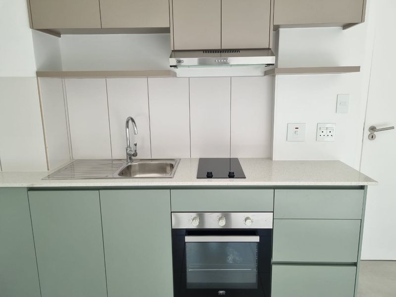 Modern kitchen featuring sage green lower cabinetry, neutral upper cabinets, stone countertops, integrated electric hob, oven, and stainless steel sink with mixer tap.