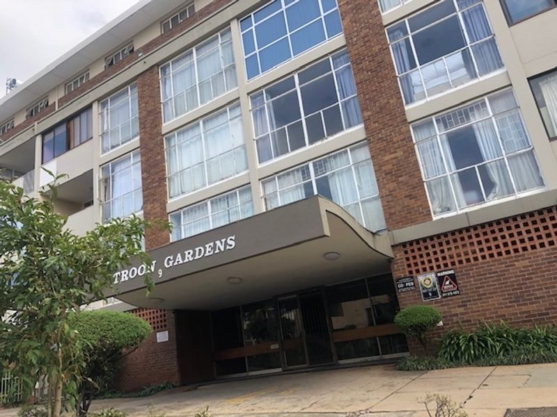 Front exterior view of Troon Gardens apartment building, featuring a brick facade, large windows, and a covered entrance area.