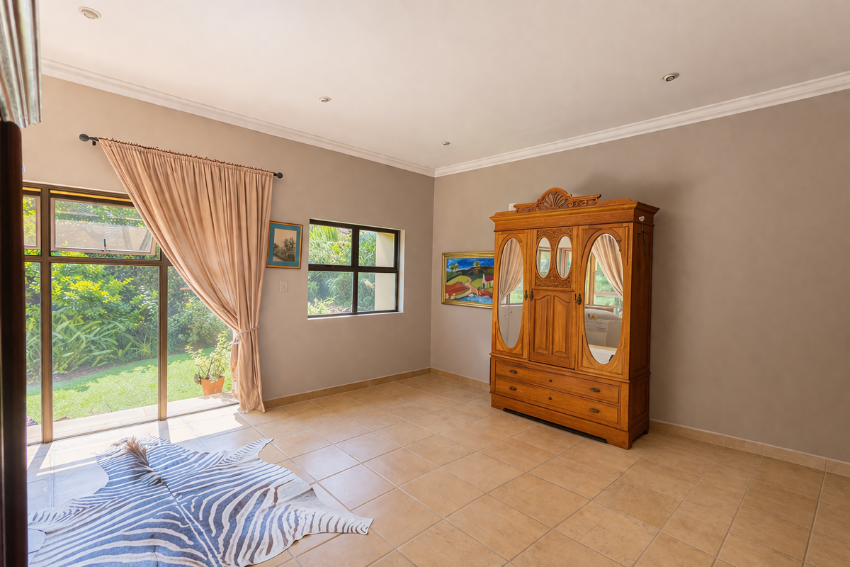 Spacious bedroom featuring neutral wall tones, tiled flooring, and large sliding glass doors providing direct access to the garden.