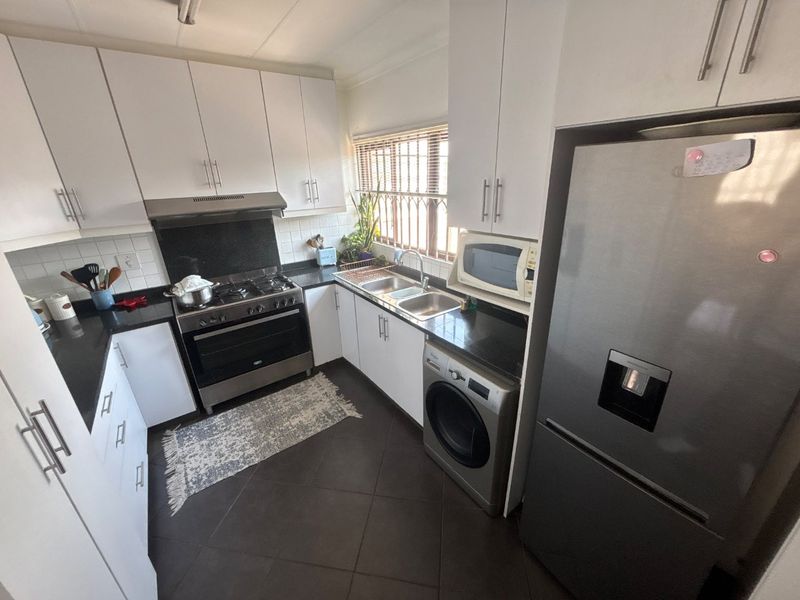 A functional kitchen featuring white cabinetry, dark countertops, a gas stove with extractor, and integrated space for a washing machine.