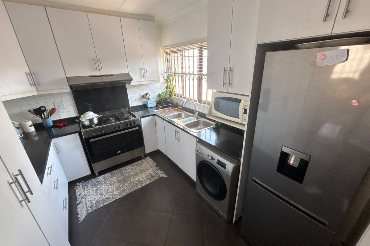 A functional kitchen featuring white cabinetry, dark countertops, a gas stove with extractor, and integrated space for a washing machine.