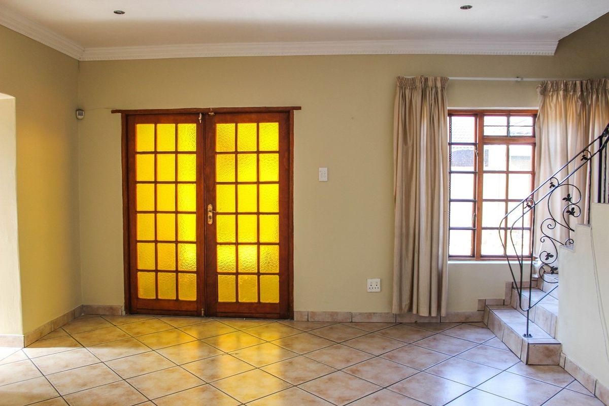 An empty living area featuring tiled flooring, wooden french doors, and a staircase with a decorative wrought iron railing.