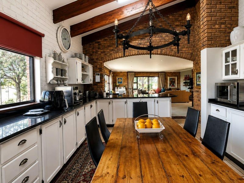 Spacious open-plan kitchen and dining area featuring exposed brick walls, timber ceiling beams, granite countertops, and a classic wrought iron chandelier.
