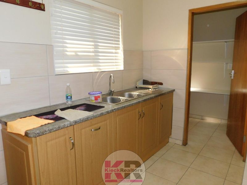 Functional scullery area featuring laminate cabinetry, double bowl stainless steel sink, stone-look laminate countertops, and tiled splashback with natural light.