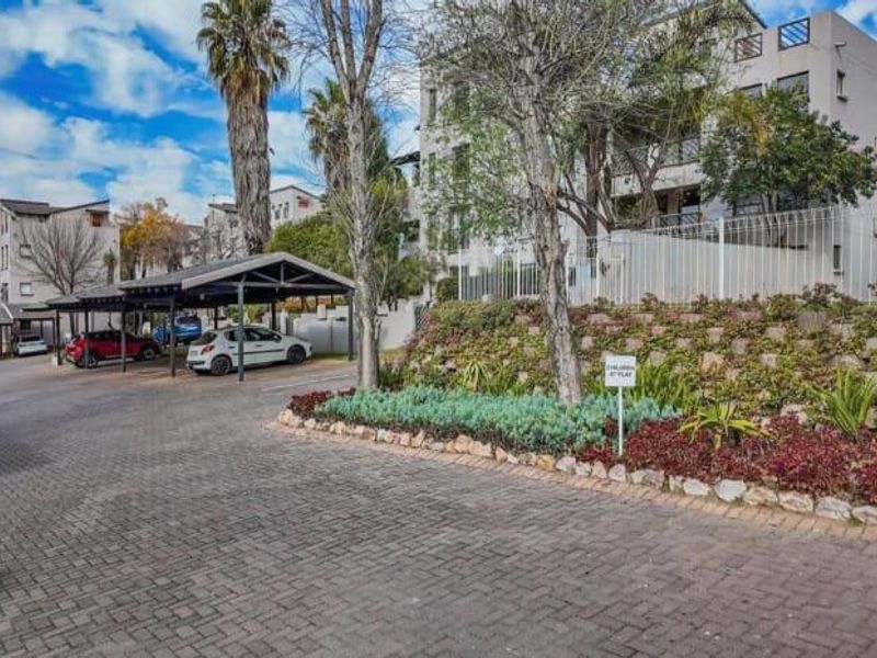 Exterior view of the apartment complex featuring a paved driveway, covered carport parking, and landscaped retaining wall garden area.