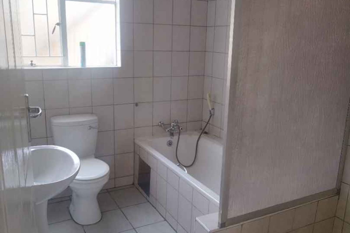 A functional bathroom featuring a pedestal basin, a standard toilet, and a combined bathtub and shower area with tiled finishes.