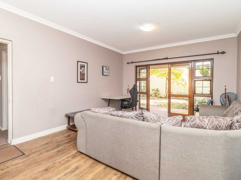 A living room featuring laminate flooring, crown molding, and wooden framed glass doors providing direct access to the outdoor area.